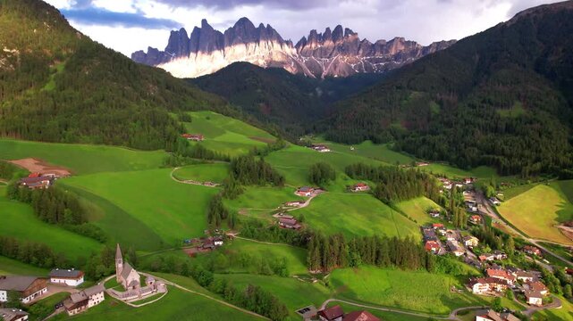 Italy Dolomites Aerial Panorama of Val di Funes Scenic Valley with Dramatic Cloudy Sky and Green Meadows Iconic Odle Geisler Peaks Mountains South Tyrol Alpine Nature Landscape Travel