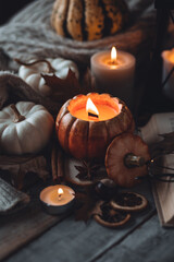Atmospheric candle - shape of pumpkins, autumn decor, book on grey fall rainy day. Autumn cozy home atmosphere, inspiration, hygge concept. Aromatherapy, warming, relaxation. Wooden background