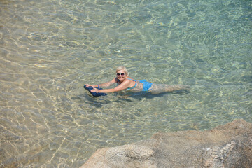Elderly woman is posing in transparent clear sea water.
