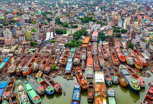 Aerial view of a dense array of colorful boats clustered along the riverbank, contrasting with the cityscape beyond, Keraniganj, Bangladesh.