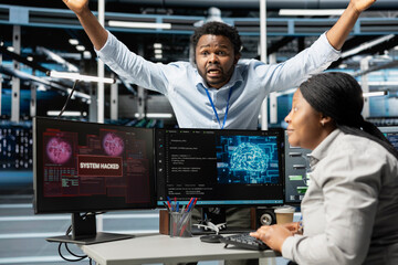 Scared server hub admins frightened by hacker passing firewall and stealing data. Security breach notification on PC monitor in data center making IT workers panic, screaming for help