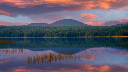 Tranquil lakeshore Sunrise landscape on a cloudy summer morning in Marshfield, Vermont, where still waters and soft light create a serene natural retreat.