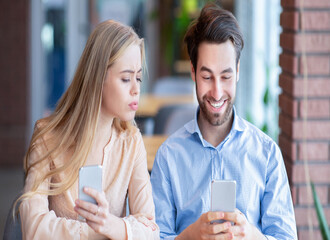 Young jealous woman looking into her boyfriend's smartphone during lunch at cafe. Millennial couple suffering from gadget addiction, neglecting each other, stuck in cellphones