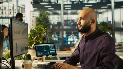 Startup staff member working to hit key performance targets for revenue, profitability and operational efficiency. Employee at computer desk doing research analysis, camera B close up