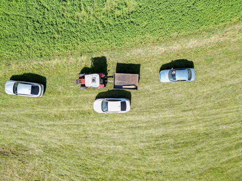 Aerial view of a red tractor amidst the lush green field, surrounded by cars, casting shadows on the vibrant landscape, Posof, Ardahan, Türkiye.
