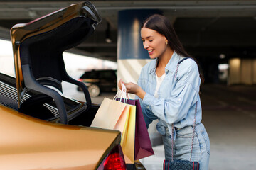 Woman putting her shopping bags into car trunk after successful shopping, ready to go home from...
