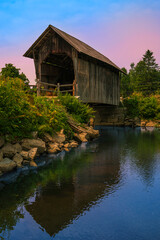 The Martin Covered Bridge, a landmark agricultural bridge built in 1890, spans the Winooski River in Marshfield, Vermont. A sunrise landscape with water reflections.