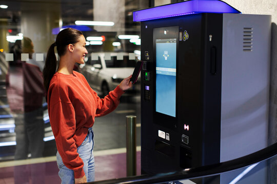 Young woman making contactless payment with smartphone at parking payment machine, parked her car at underground parking in shopping mall