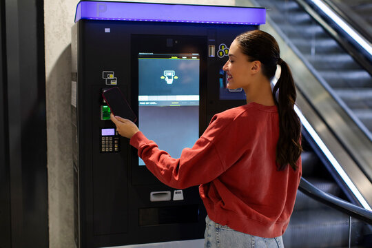 Young woman paying for service underground parking or buying a subway or train ticket using electronic self-service kiosk
