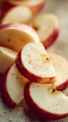 Close-up of sliced red apples with creamy flesh, arranged on a speckled, neutral surface