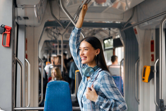 Lady holding handle, standing in public transport, enjoying trip at city modern tram, looking at window and smiling, free space