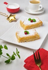 Dessert, lemon shortcrust pastry bars sprinkled with powdered sugar, on a white rectangular plate on a light concrete background. Lemon pastries.