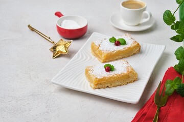 Dessert, lemon shortcrust pastry bars sprinkled with powdered sugar, on a white rectangular plate on a light concrete background. Lemon pastries.