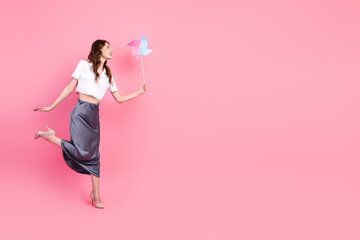 Young woman holding a colorful pinwheel on a pink background in an elegant skirt and stylish white shirt