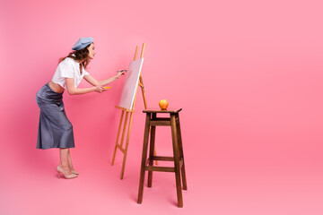 Elegant young artist painting on a pastel pink backdrop, embracing creativity and self-expression during a leisure moment
