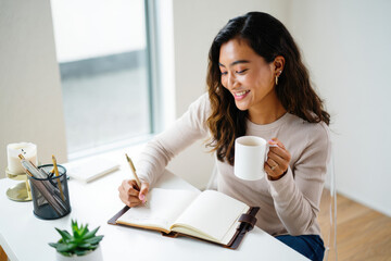Smiling woman plans her day while enjoying coffee in bright workspace for wellness blog