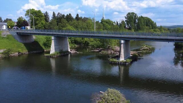 Video filmed by a drone passing under a road bridge, between concrete pillars at the edge of the forest under a cloudy sky.