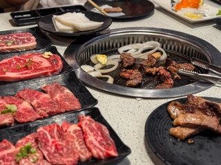 Assorted Korean BBQ meats on a sizzling hot plate, surrounded by side dishes and dipping sauces, showcasing traditional Korean cuisine in a vibrant dining setting.