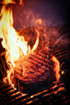 Barbecue dry aged angus tomahawk steak close-up on a charcoal grill with fire and smoke