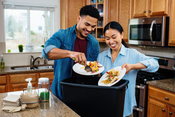 Smiling couple composting food waste at home to reduce environmental impact and live sustainably
