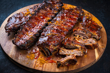 Barbecue smoked hot spicy pork spareribs St Louis cut with curry rub and BBQ sauce on wooden cutting board