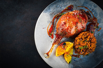 Traditional barbecue gourmet duck haunch with mushroom risotto and orange slices served with spicy chili sauce as top view on a design plate