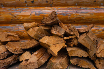 Pile of chopped firewood stacked against a rustic log wall, ready for use as heating fuel. Detailed texture of dry wood and tree rings. Warm earthy tones, traditional cabin background. No people 
