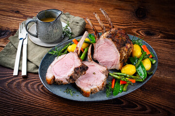 Juicy dry aged bone-in back rack of pork loin roast served as close-up with herbs and vegetable mix on a Nordic design plate
