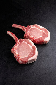 Raw dry aged trimmed bone-in pork loin chops cutlets offered as close-up on a black board