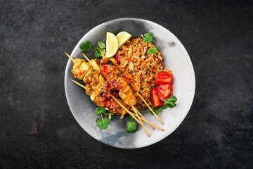 Authentic sate ayam - grilled chicken satay sate skewers with stir-fried rice and vegetable served as top view on a design plate