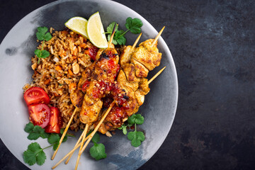Authentic sate ayam - grilled chicken satay sate skewers with stir-fried rice and vegetable served as top view on a design plate