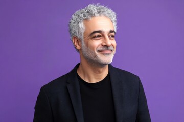 Fototapeta premium A confident and poised man in a professional setting. Modish men's textured crop haircut - midlife arabian man with curly hair. Concept art of style for aging men. Purple solid background.