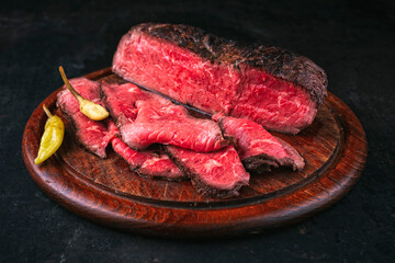 Traditional barbecue dry aged sunday roastbeef as cold cuts served as close-up on a wodden cutting board