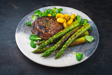 Grilled green asparagus with beef burger patty, gnocchi and fresh green salad served as closeup on a design plate