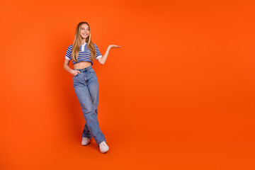 Happy young woman smiling in trendy striped top and jeans posing against an orange backdrop displaying cheerful attitude