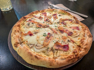 Top view of freshly baked Italian pizza topped with melted cheese and ham placed on restaurant's dinning table
