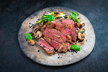 Traditional barbecue grass-fed dry aged roast beef steak  served as close-up with mushrooms and greens on a rustic design plate