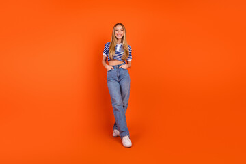 Young stylish woman posing confidently on vibrant orange background with a casual trendy outfit in striped shirt and jeans