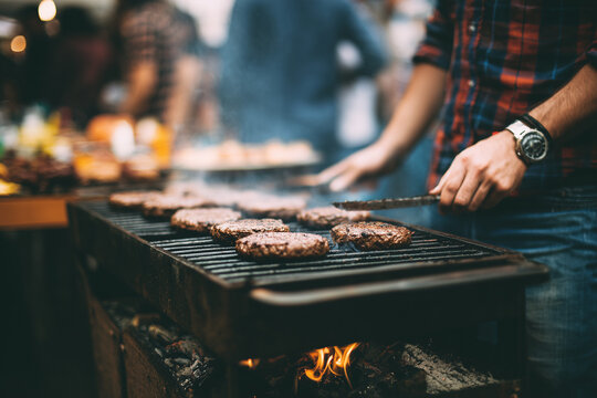Man grilling juicy burgers on a smoky barbecue outdoor