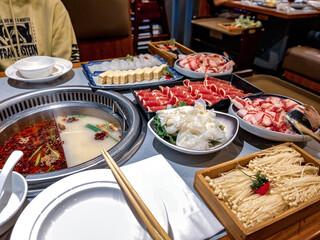 Traditional Chinese hot pot with a variety of meats, tofu, mushrooms, and vegetables in spicy and milky broths.