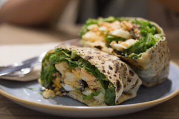 Caesar salad wrapped with bread filled with green lettuce, croutons, eggs, and salmon. Cut in two and plated in a pretty way