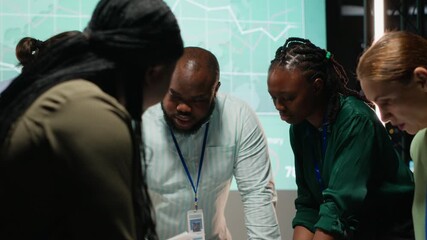 Diverse project team meeting after hours to share data visualization reports, discuss business intel and prepare forecasts for upcoming presentations to enterprise shareholders after hours. Camera B. - Powered by Adobe