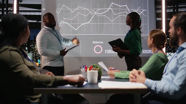 African american manager presenting monthly financial situation during night time meeting, reviewing resources available for a new project. Shareholders discuss possibilities. Camera A.