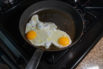 view of two fried eggs sizzling in a pan on a stovetop
