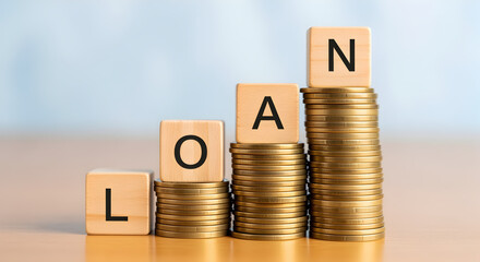 Stacks of Golden Coins and Wooden Blocks Arranged to Spell Loan in Ascending Order on Tabletop Against Blurred Background