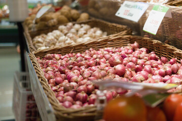 Display of red onion, tomato, garlic, and potato on a brown crate with a blurred background ready to sell in supermarket