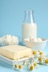 Fresh dairy products and chamomile flowers on light blue background, closeup