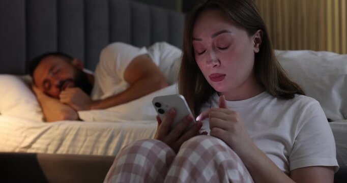 Betrayal. Jealous woman finding proofs of her unfaithful husband on smartphone while he sleeping and awaken him in bedroom