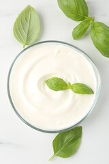 Tasty yoghurt with basil in bowl on white table, flat lay