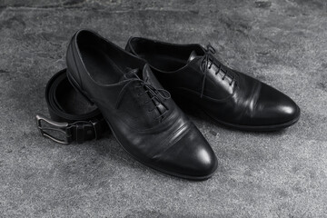 Pair of black leather shoes and belt on grey surface
